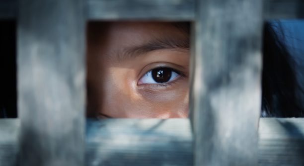 The blank stare of a child's eye who is standing behind what appears to be a wooden frame
