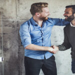 Young happy businessmen talking while shaking hands in the office.